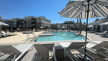 A pool area with sun loungers and a striped umbrella at The Quinn Luxury Apartments, Pensacola, FL, 32526